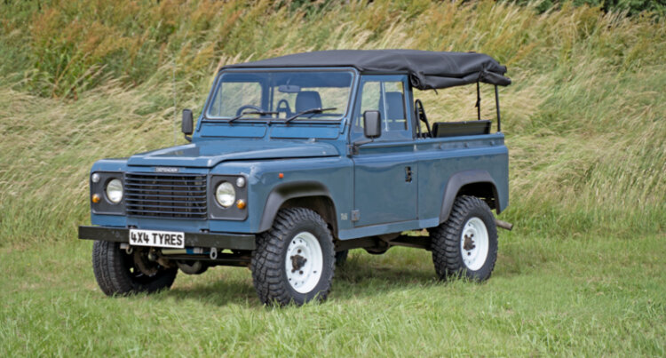 A blue classic land rover sat on white wolf steel wheels in a field