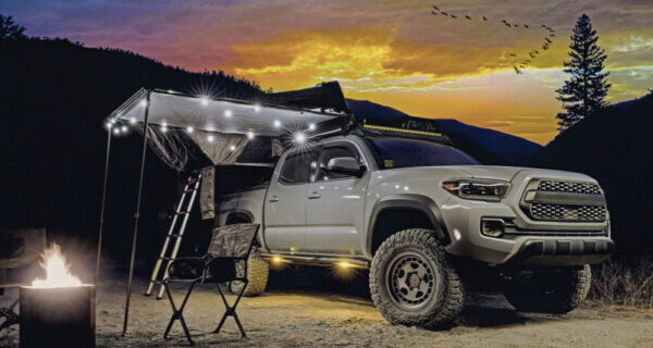 Off-road pickup with camping awning and rooftop gear at sunset