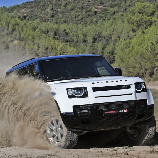 A white Land rover sat on General tires throwing up a load of mud