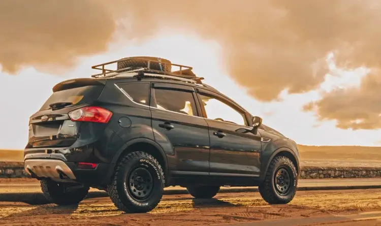 A Ford Kuga sat on a beach. It shows its overlanding ability with it steel wheels and tyres