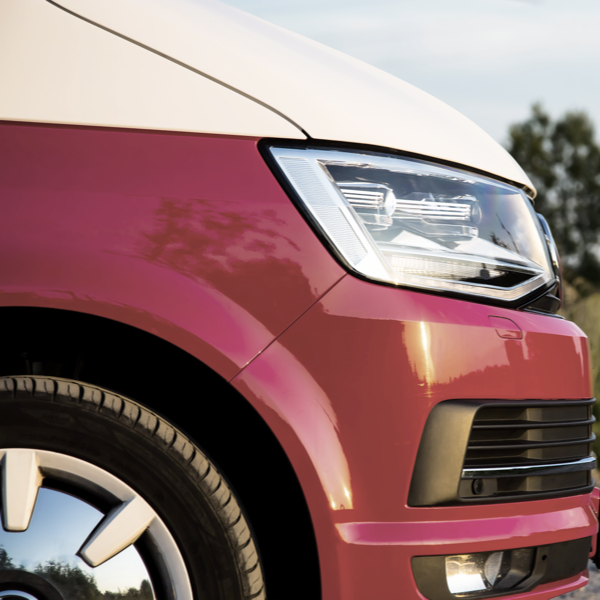 Close-up of a red van showing the front wheel, tyre and headlight.
