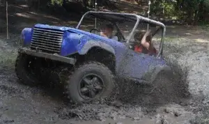 Blue Land Rover-based CCV trials car competing through a deep muddy section