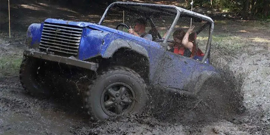 Blue Land Rover-based CCV trials car competing through a deep muddy section