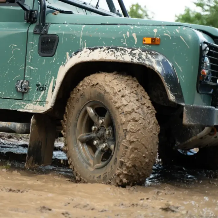 Land Rover Defender with a mud-covered tyre on muddy ground at Whitecliff Off Road Centre.