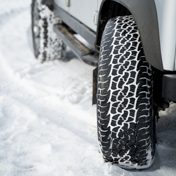Close-up of a 4x4 tyre with snow in its tread, standing on a snow-covered surface.